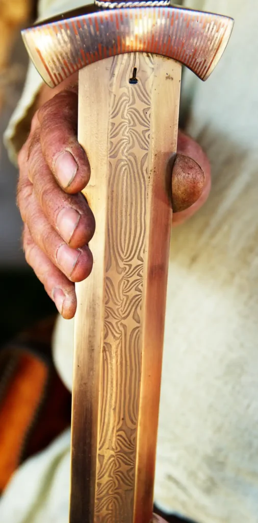 Detail van een gedamasteerde kling: in de geul wordt het visgraatpatroon zichtbaar dat ontstaat door het in elkaar smeden, splijten en draaien van strips ijzer en staal. Foto: Wikimedia Commons (Ejvind Nørgård, Pattern Welded Sword Blade).